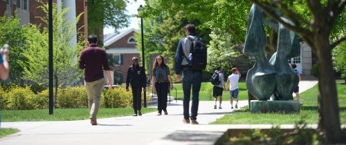 Multiple students walking to class on a sunny day near the flame statue