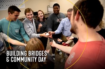Students, faculty, and staff standing in a circle with hands inside circle touching rock participating in exercise for building bridges